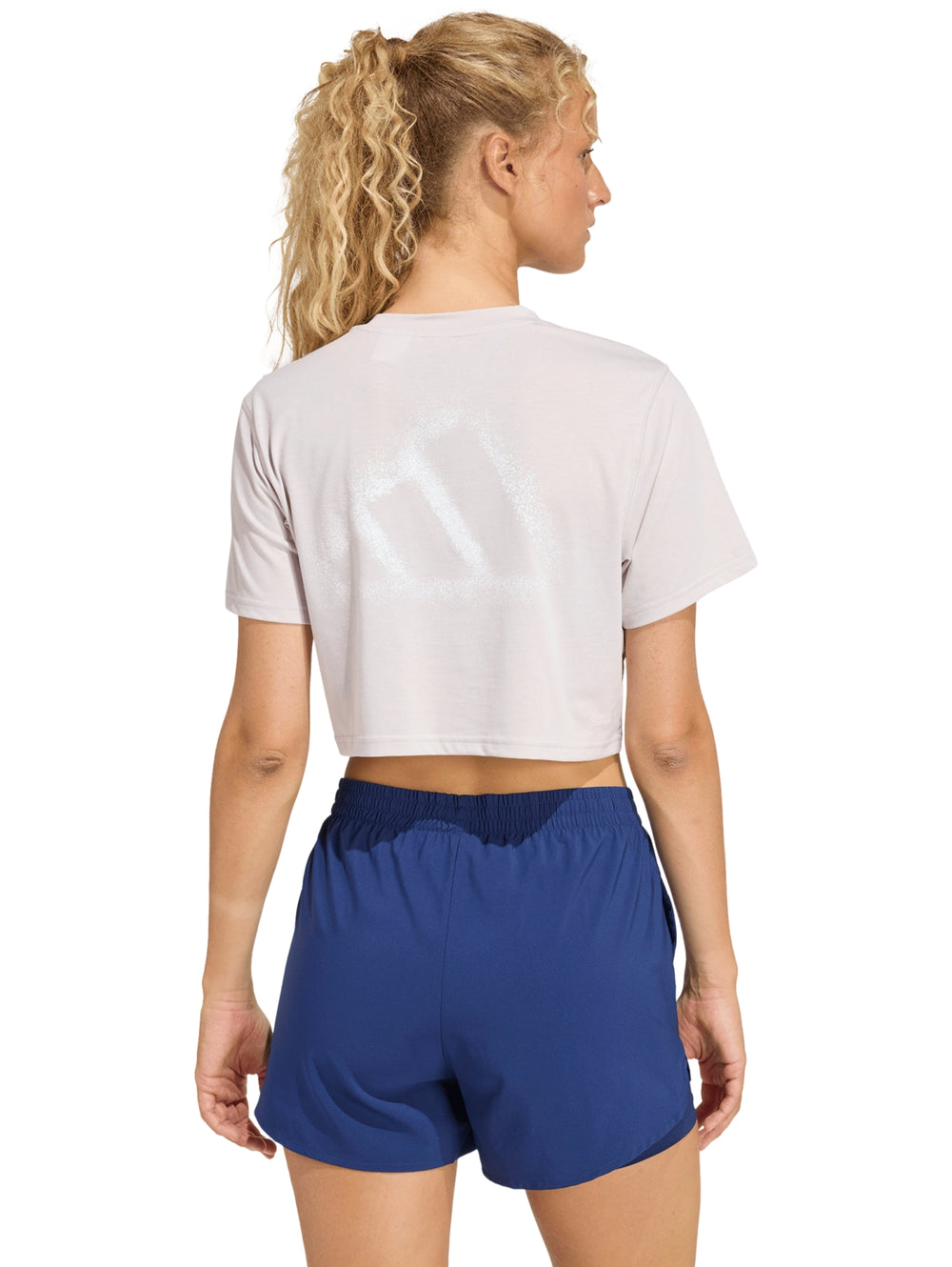 Mujer modelando una camiseta deportiva corta color violeta claro de la marca Adidas.