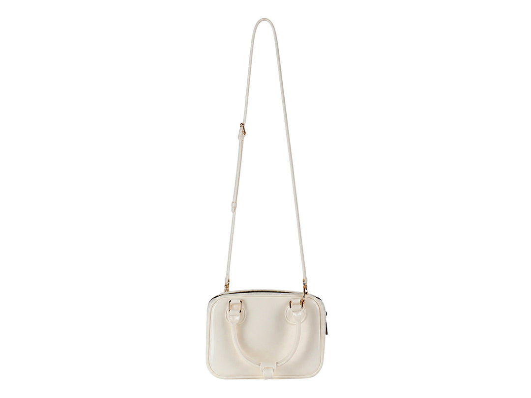 Bolsa de mano color latte con acabado brillante y detalles metálicos dorados.