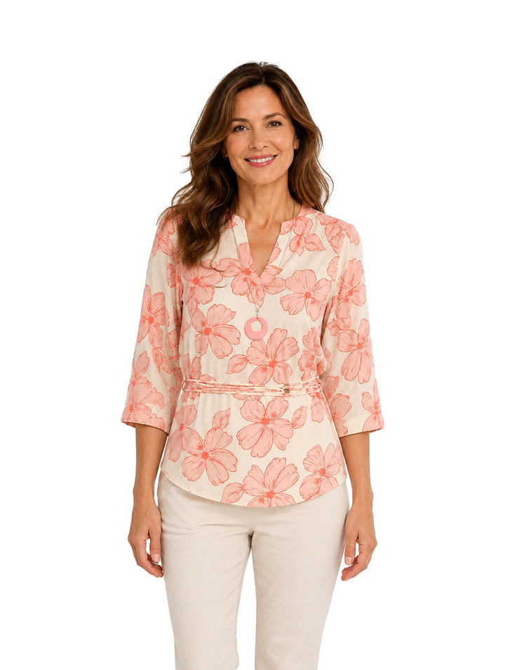 Mujer vistiendo blusa color coral y crema con estampado floral y collar circular.