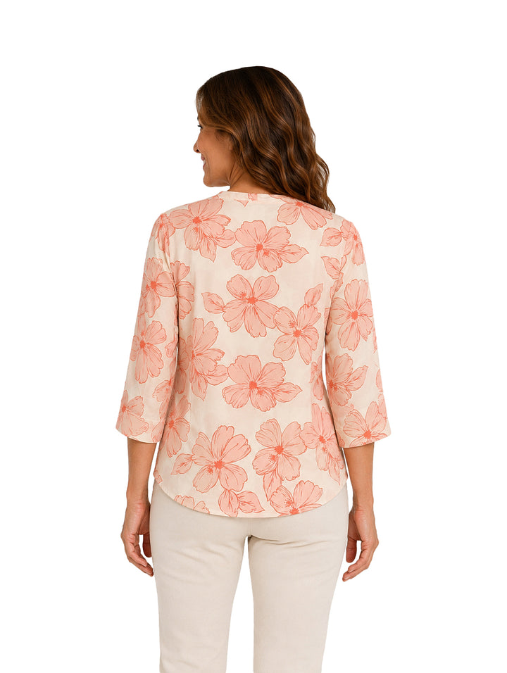 Mujer vistiendo blusa color coral y crema con estampado floral y collar circular.