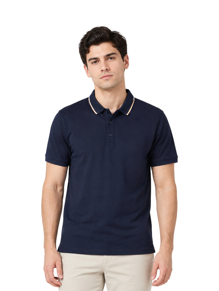 Hombre vistiendo playera polo color marino con detalle beige en el cuello y pantalones beige.