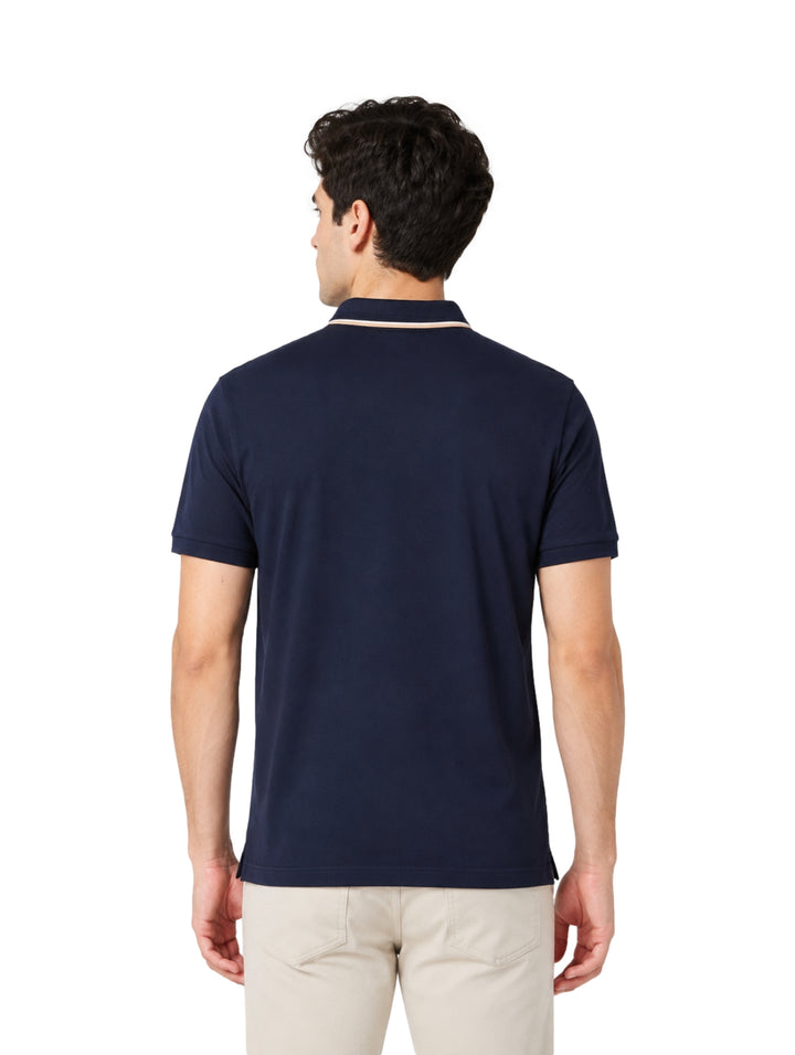 Hombre vistiendo playera polo color marino con detalle beige en el cuello y pantalones beige.