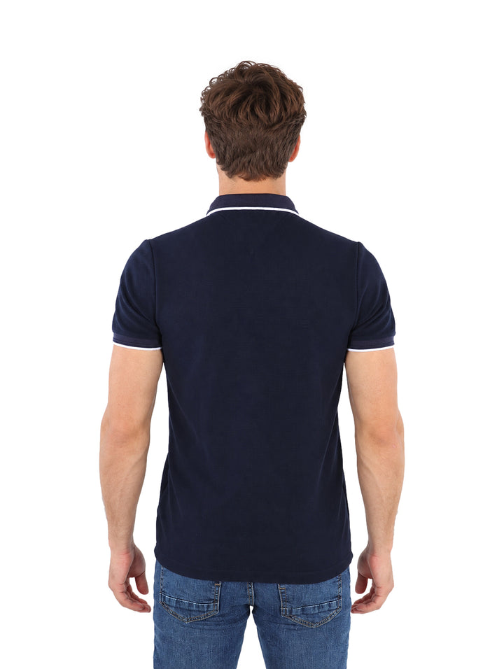 Hombre vistiendo playera polo color marino con detalles blancos en el cuello y mangas.
