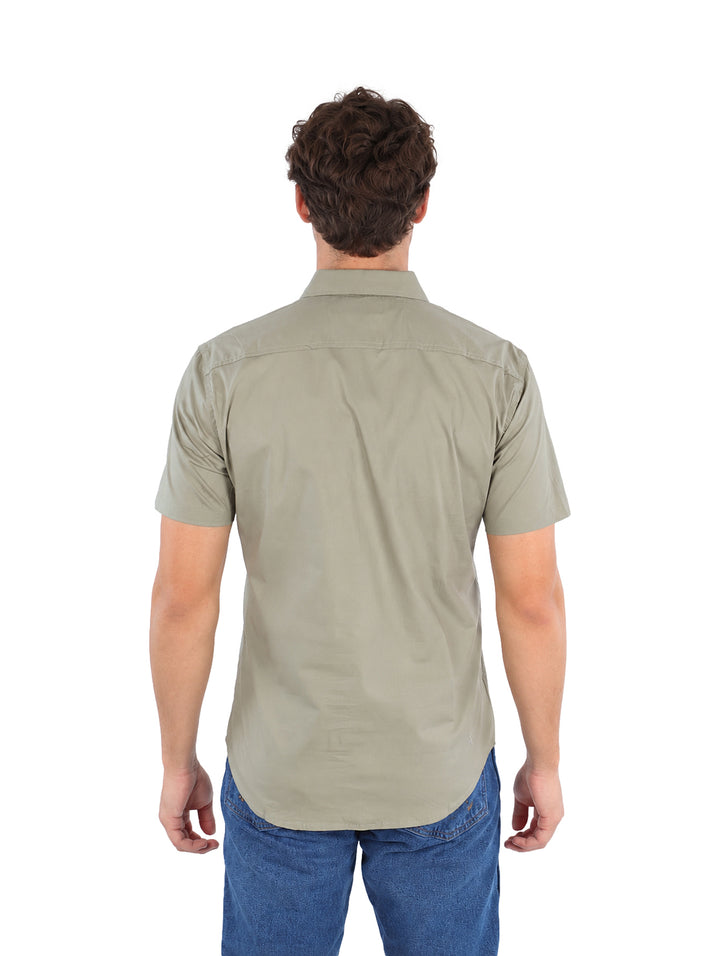 Hombre vistiendo una camisa de manga corta color olivo y pantalones vaqueros azules sobre fondo blanco.
