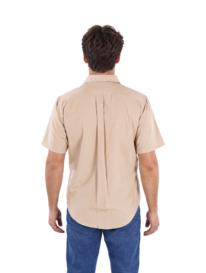 Hombre vistiendo una camisa de manga corta color arena con botones y un bolsillo en el pecho.