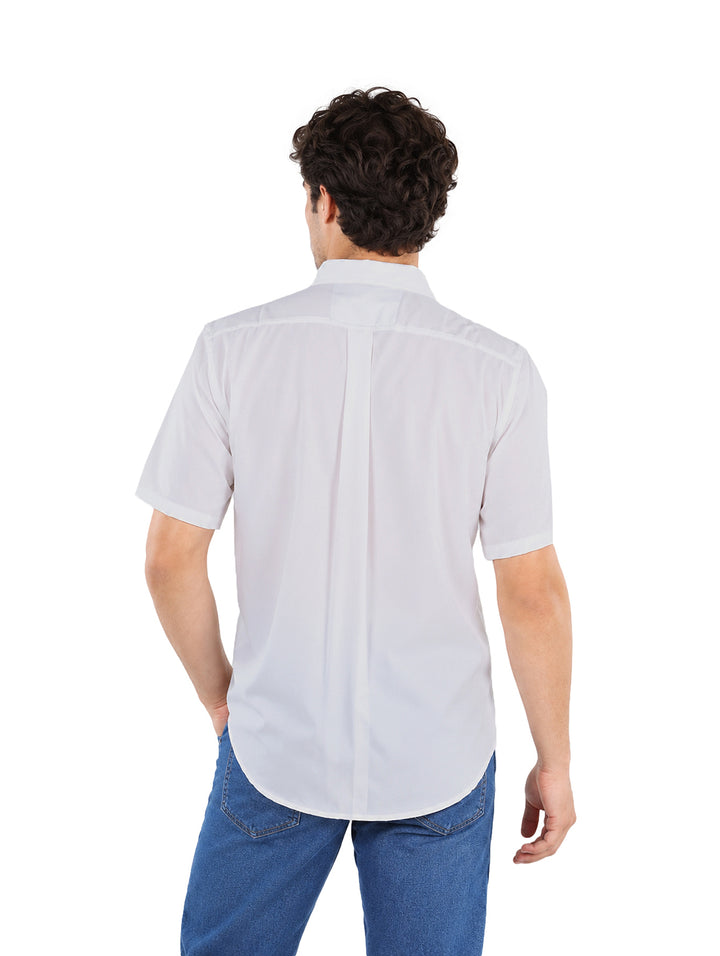 Hombre vistiendo una camisa blanca de manga corta con bolsillo frontal y pantalones azules.