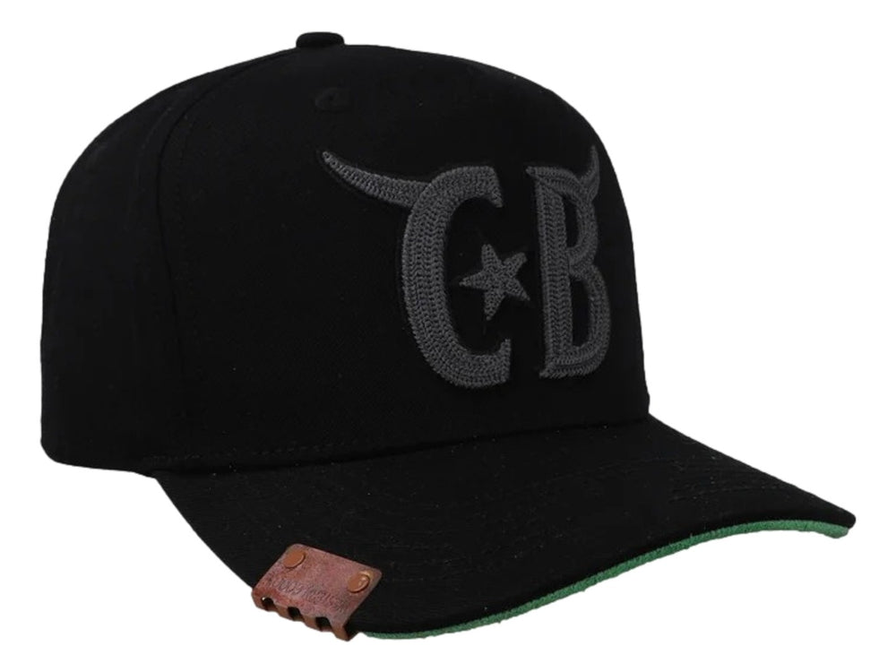 Gorra negra Cara Blanca con bordado gris de cuernos y letras CB, visera con borde verde y detalle lateral en cuero.