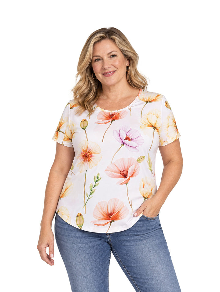 Mujer vistiendo blusa blanca de manga corta con estampado de flores en tonos naranja, amarillo y rosa.
