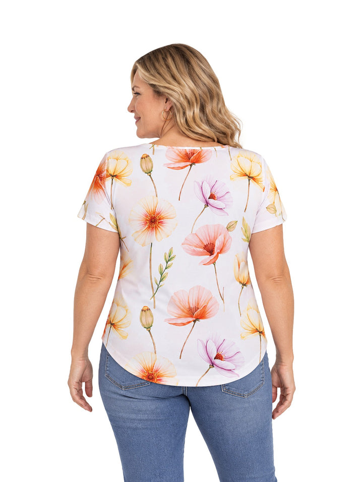 Mujer vistiendo blusa blanca de manga corta con estampado de flores en tonos naranja, amarillo y rosa.