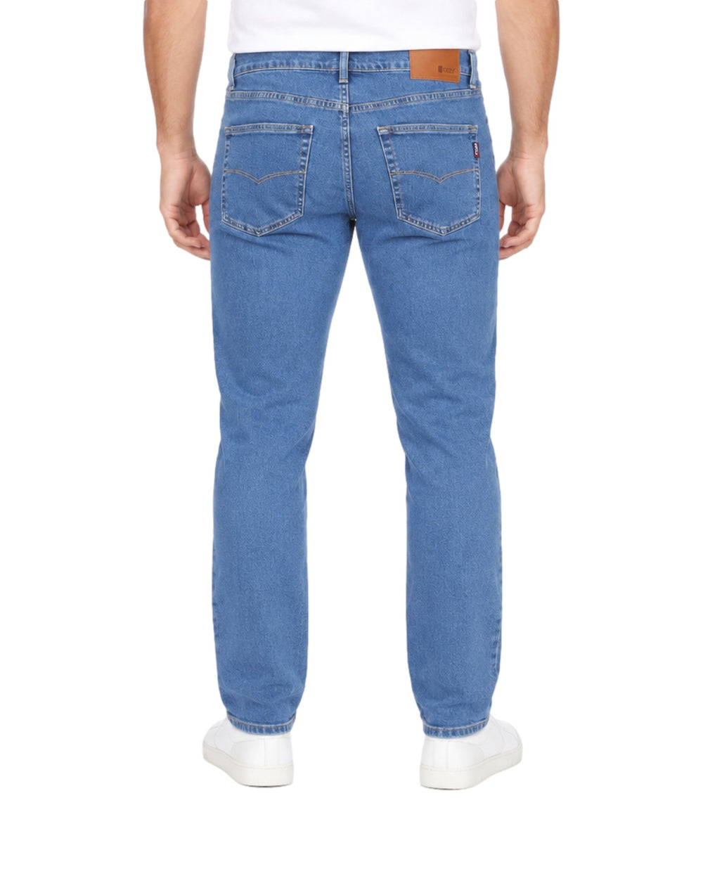 Hombre vistiendo jeans OGGI color stone blue con tenis blancos sobre fondo blanco.