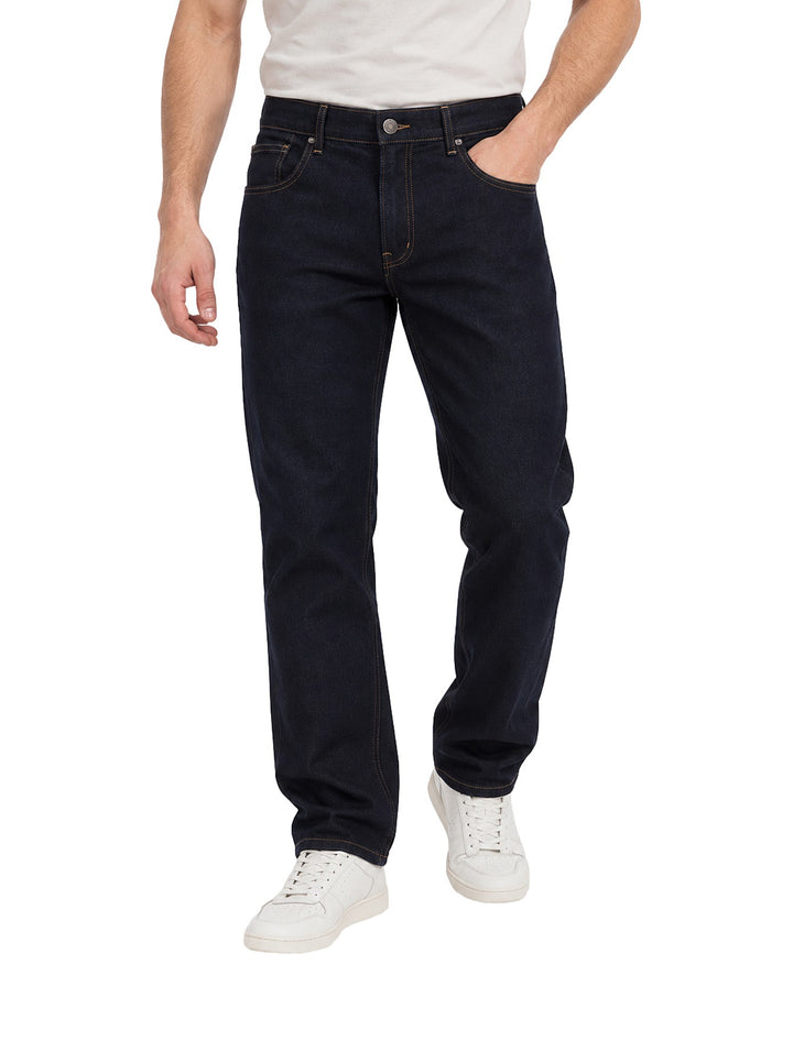 Hombre vistiendo jeans OGGI color dark indigo de corte recto con costuras naranjas y tenis blancos.