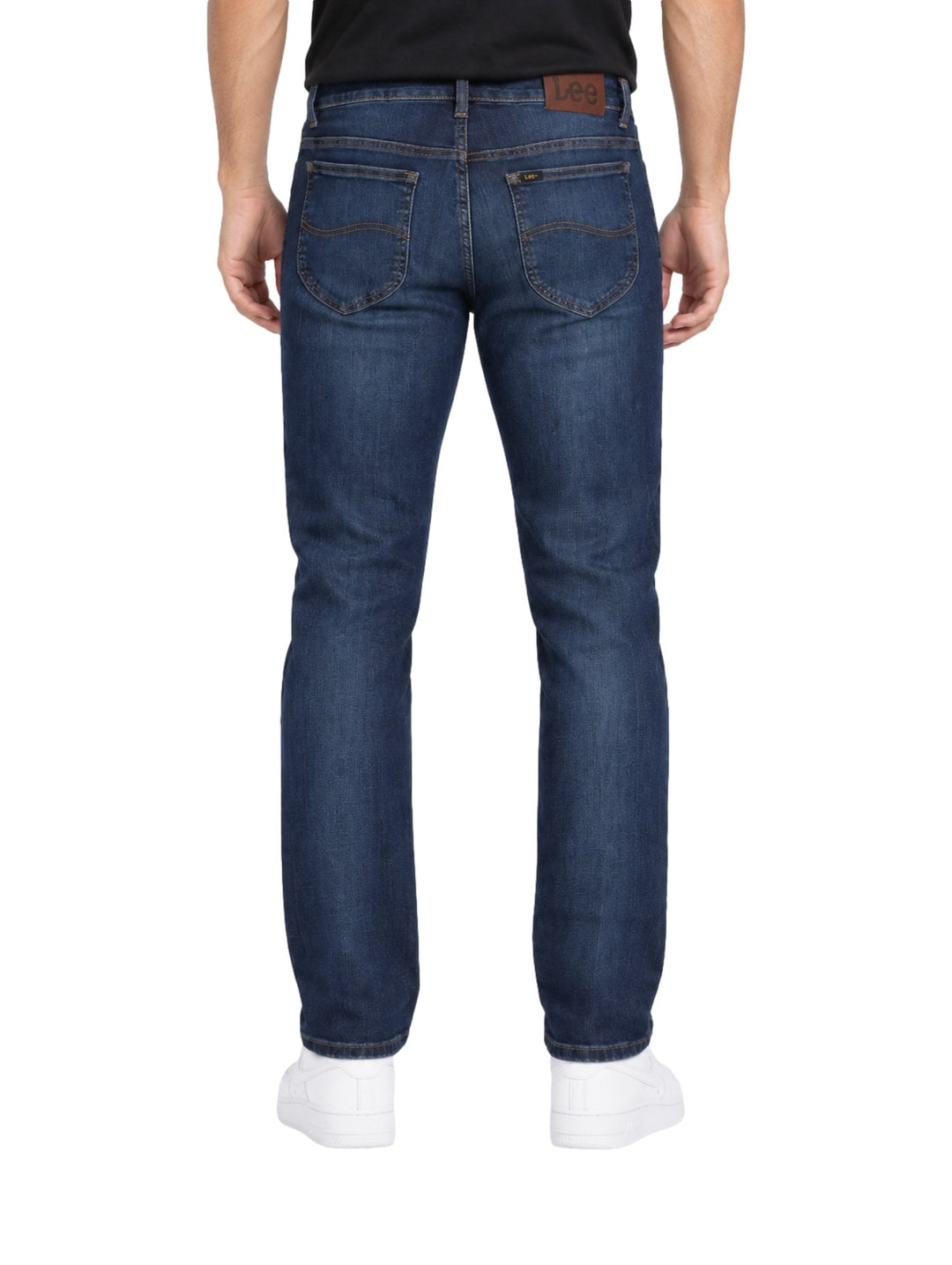 Hombre vistiendo jeans slim fit Lee color azul stone con tenis blancos sobre fondo blanco.