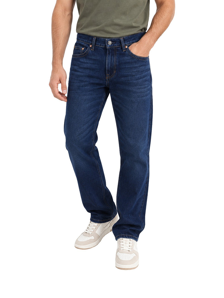 Hombre vistiendo jeans slim boot retro Wrangler en color azul oscuro con tenis blancos.