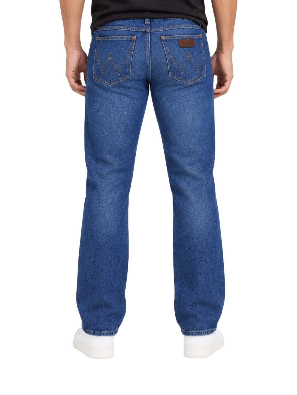 Hombre vistiendo jeans slim boot retro Wrangler en color azul con calzado blanco.