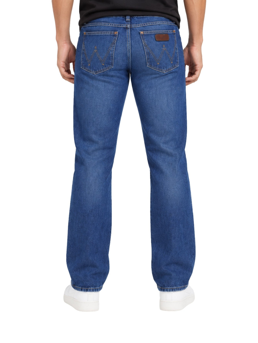 Hombre vistiendo jeans slim boot retro Wrangler en color azul con calzado blanco.