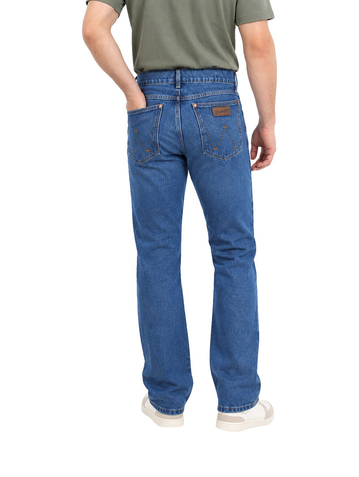 Hombre vistiendo jeans Wrangler color indigo de corte slim boot retro con calzado blanco.