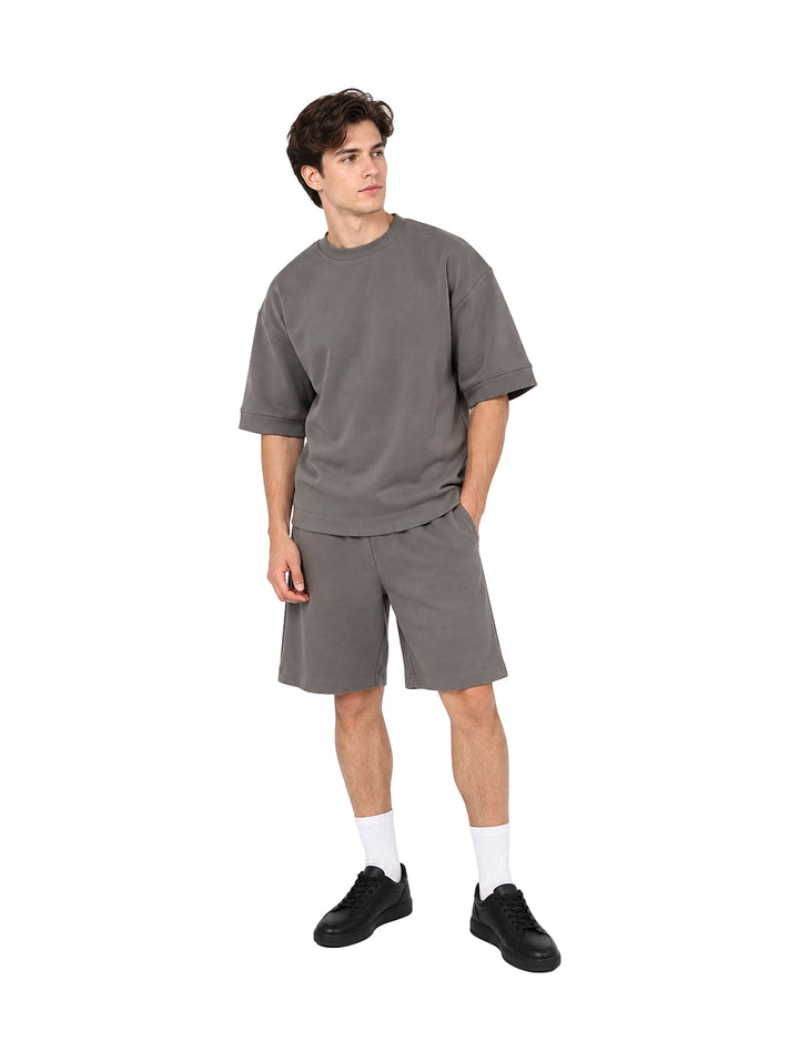 Hombre vistiendo un conjunto de camiseta y shorts color gris de estilo casual y holgado.