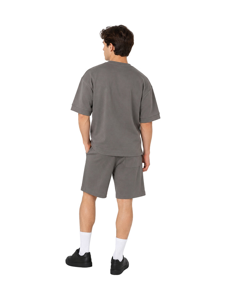 Hombre vistiendo un conjunto de camiseta y shorts color gris de estilo casual y holgado.