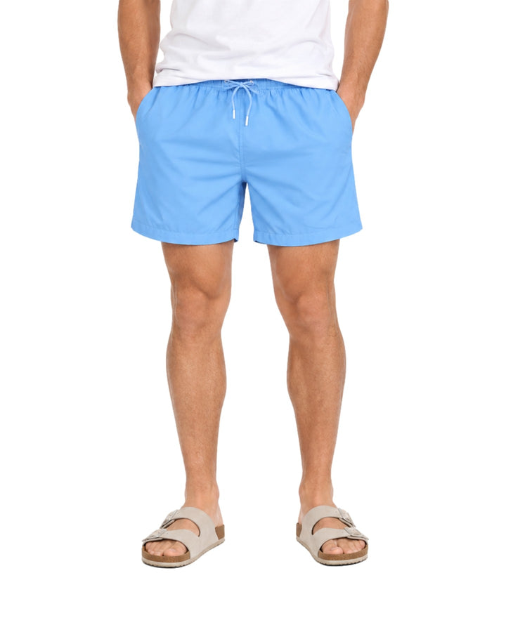 Hombre vistiendo un traje de baño corto color azul de la marca American Fly con cordón ajustable en la cintura.