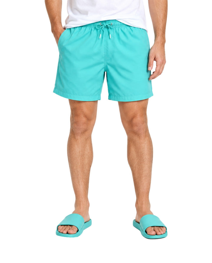 Hombre vistiendo un traje de baño corto color verde menta con cordón ajustable y sandalias a juego.