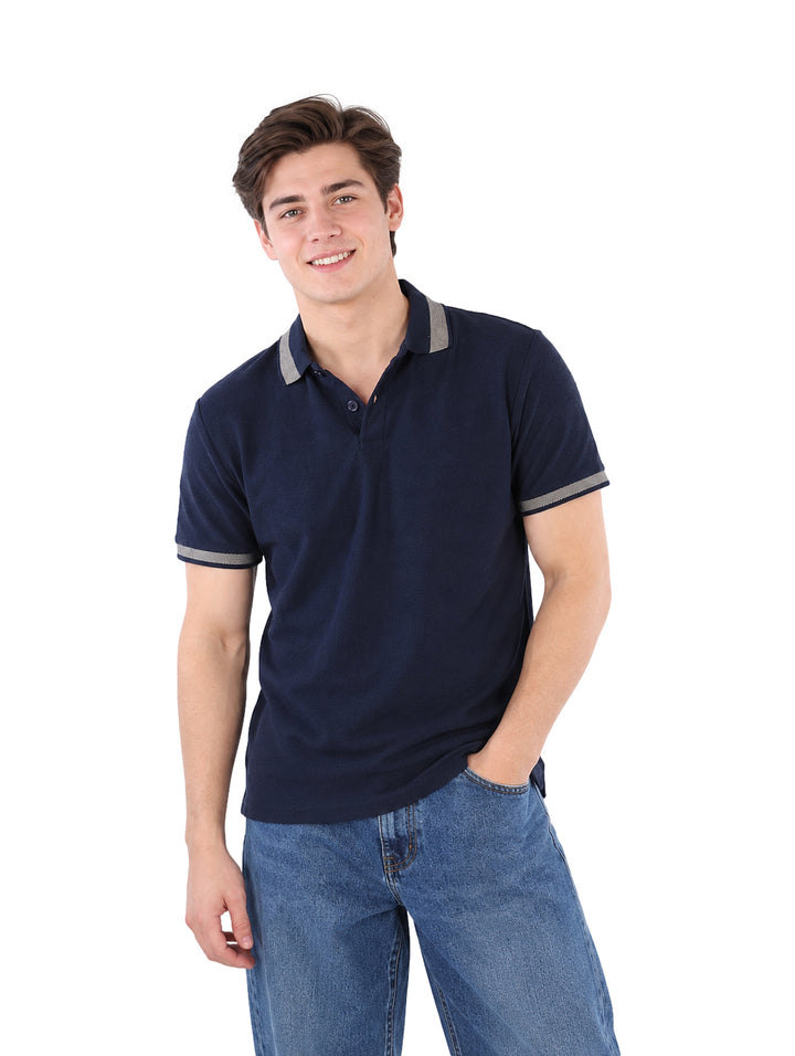 Hombre vistiendo playera polo color marino con detalles en gris en el cuello y mangas.