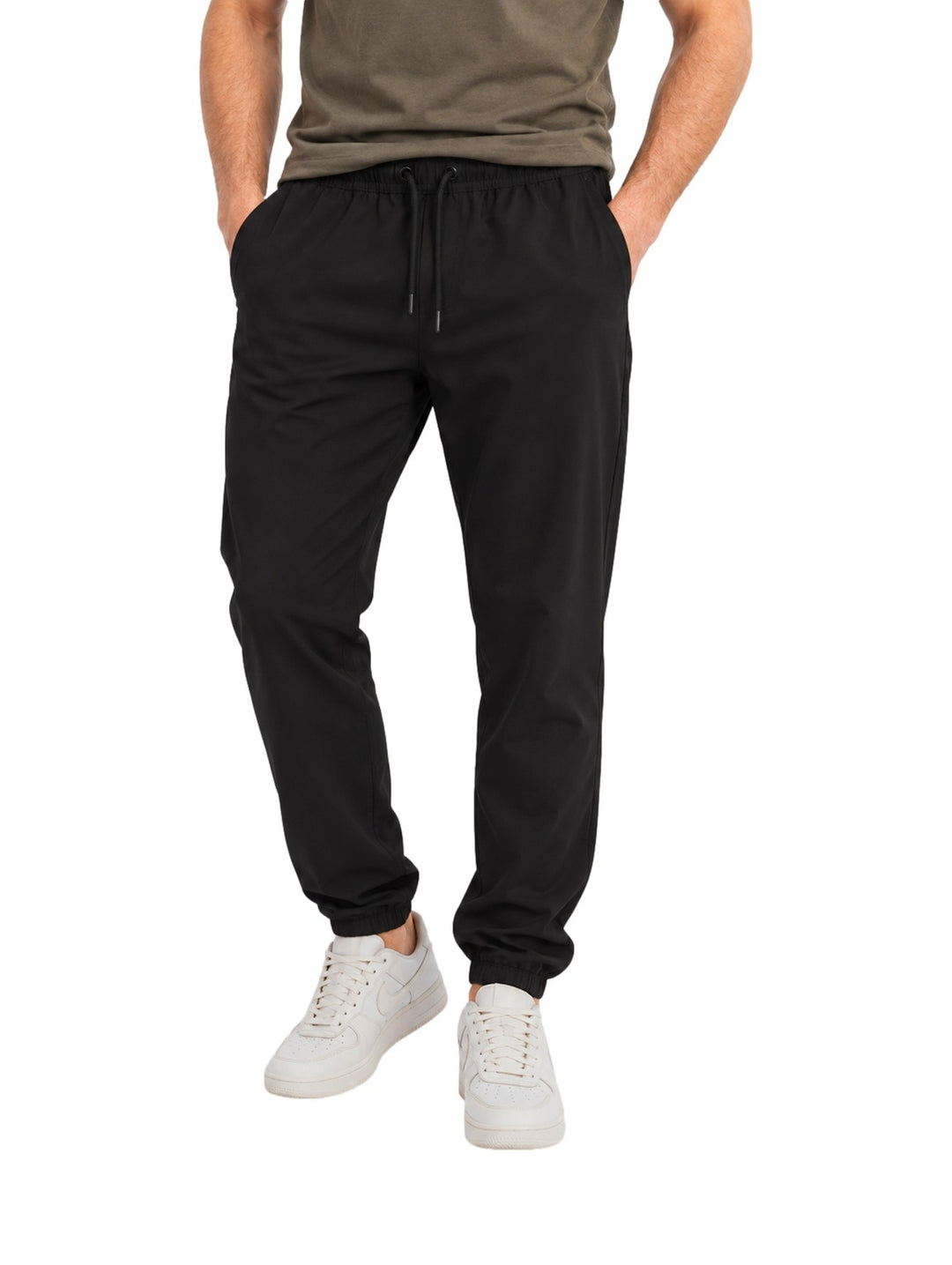 Hombre vistiendo pantalón American Fly negro de corte elástico con tenis blancos sobre fondo blanco.