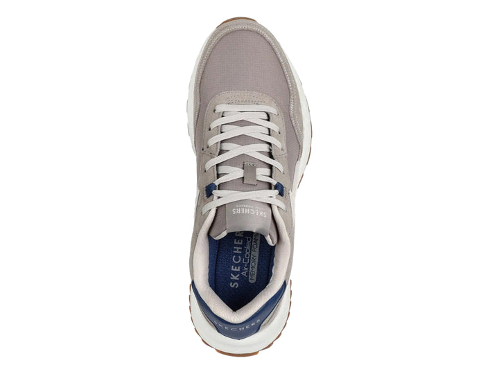 Tenis Skechers color gris natural con suela blanca y detalles en azul y café.
