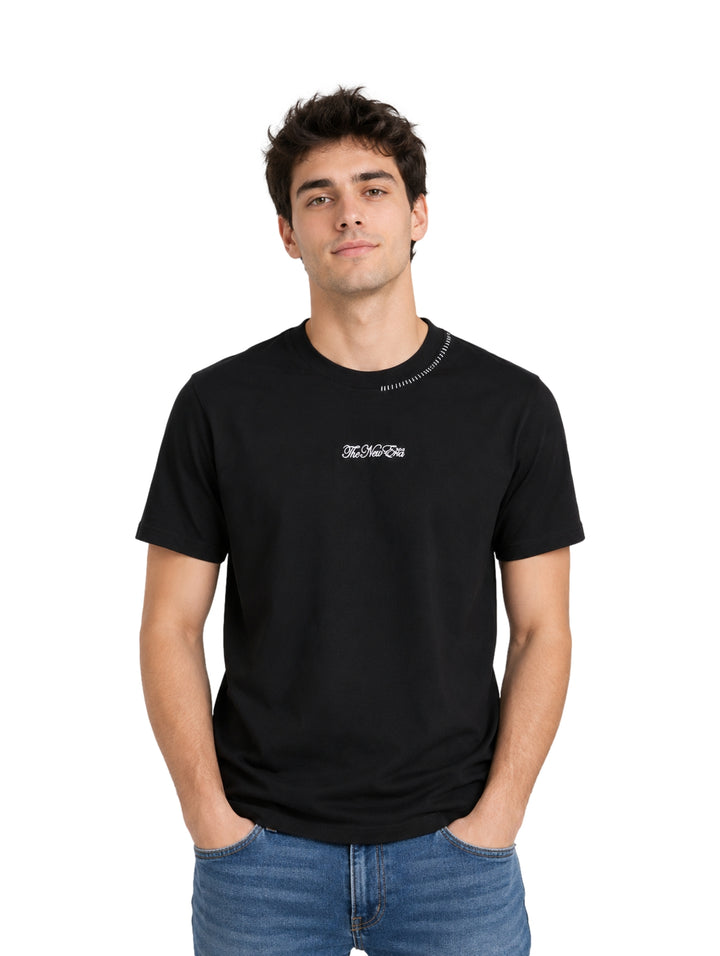 Hombre usando una playera negra de manga corta con un pequeño detalle blanco en el pecho y cuello.