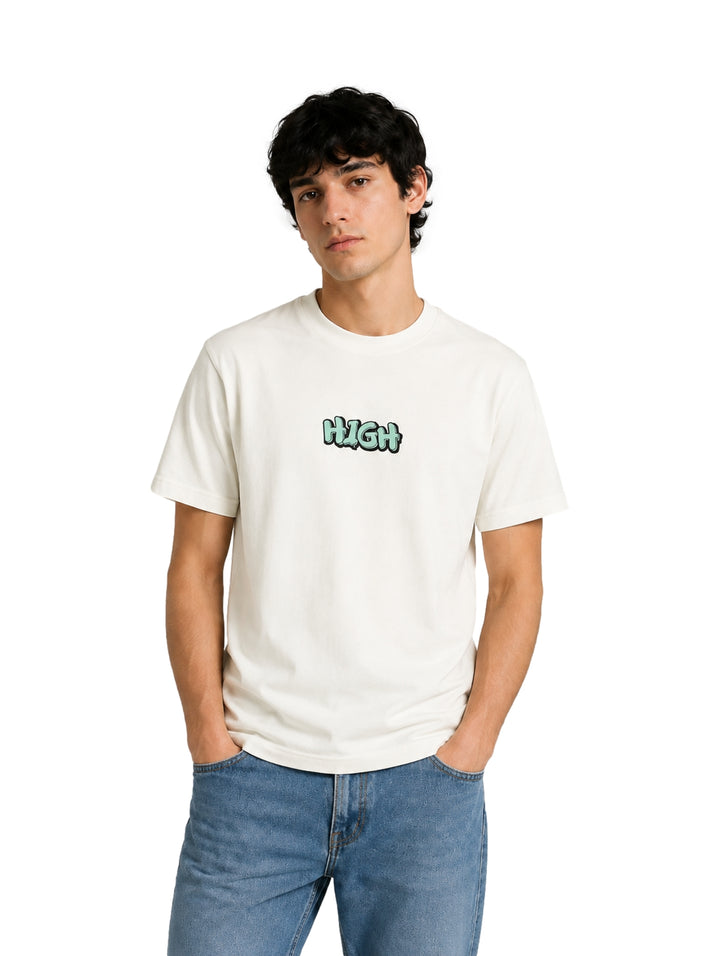 Hombre usando playera blanca de manga corta con estampado pequeño en el centro y jeans azules.