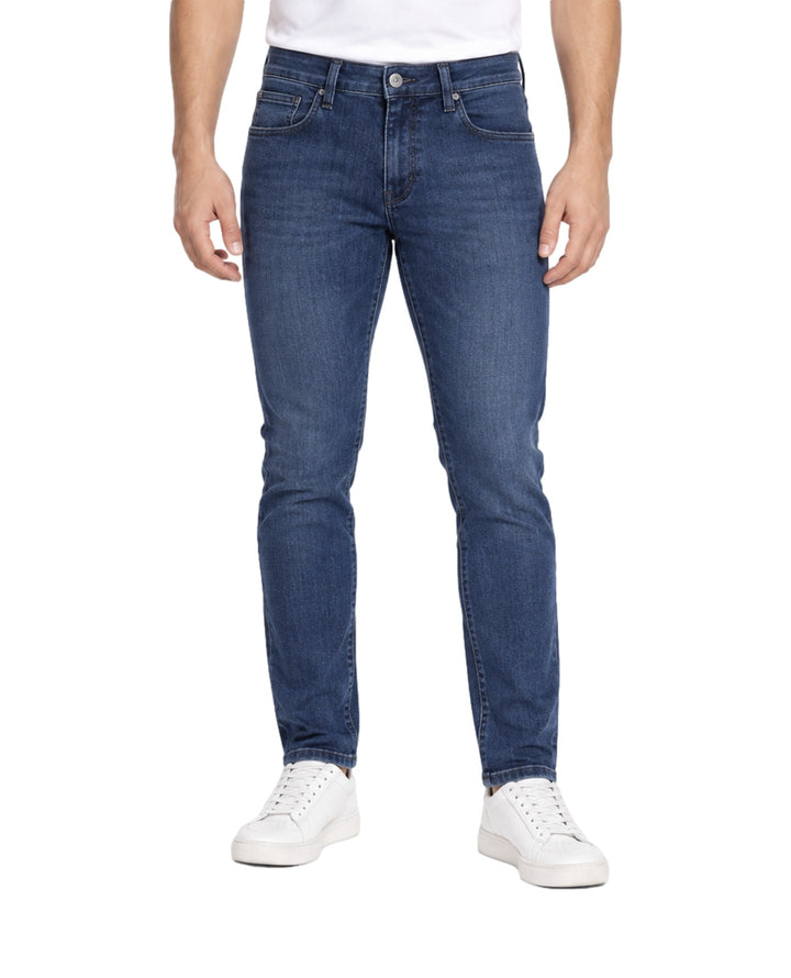Hombre vistiendo jeans slim fit color índigo con tenis blancos sobre fondo blanco.