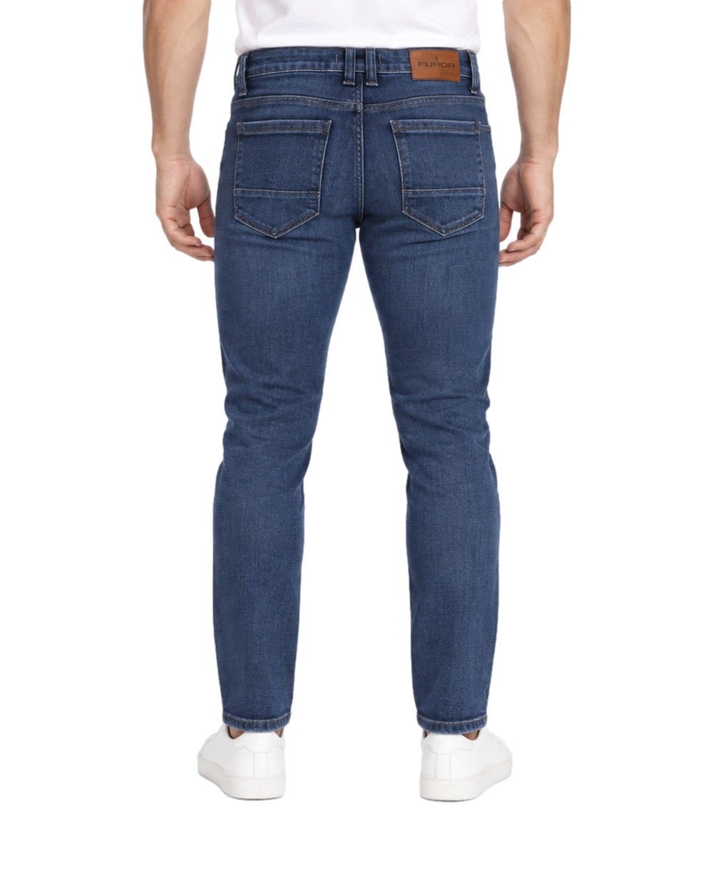 Hombre vistiendo jeans slim fit color índigo con tenis blancos sobre fondo blanco.