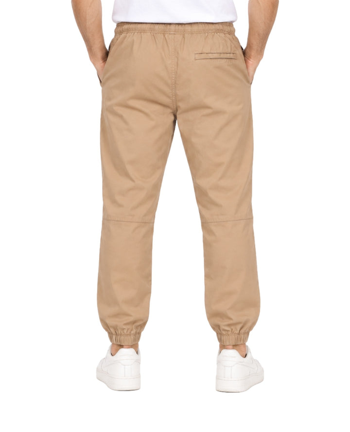 Hombre vistiendo pantalones jogger color khaki con cintura y tobillos elásticos y tenis blancos.