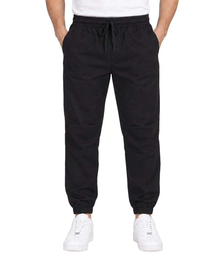 Hombre vistiendo pantalón jogger deportivo color negro con cintura elástica y calzado blanco.