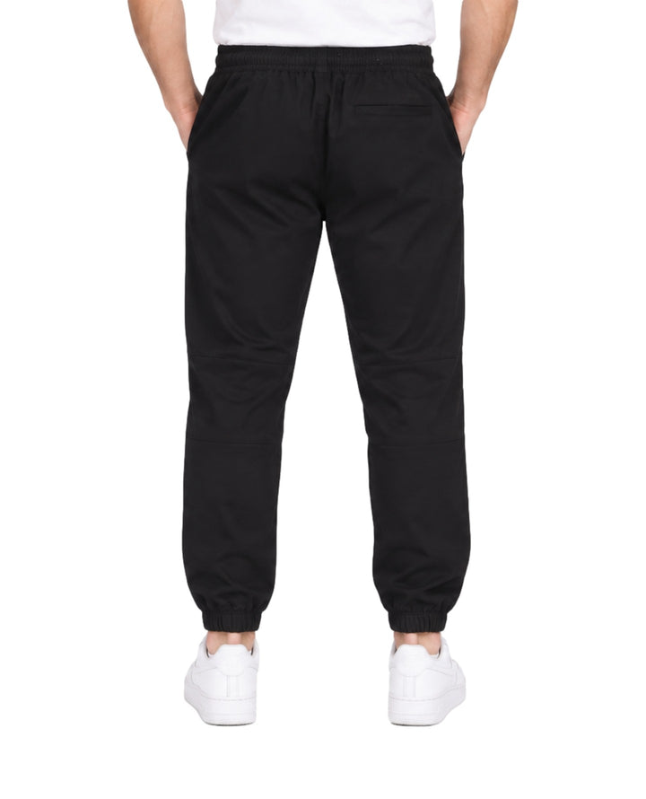Hombre vistiendo pantalón jogger deportivo color negro con cintura elástica y calzado blanco.