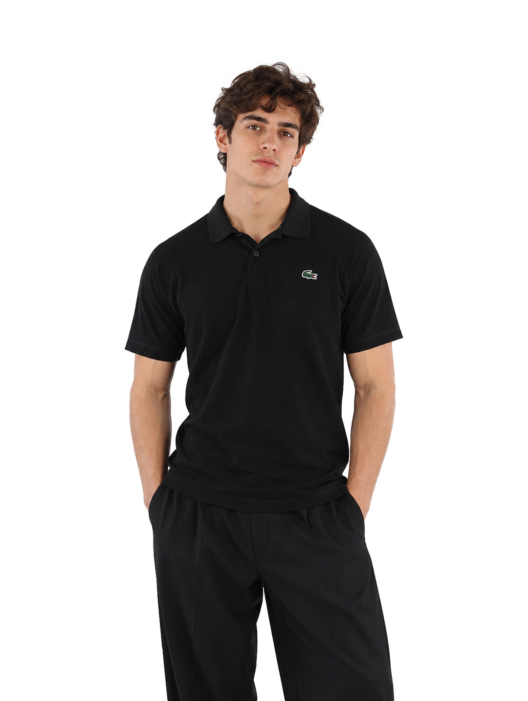 Hombre vistiendo playera polo Lacoste color negro y pantalones negros sobre fondo blanco.