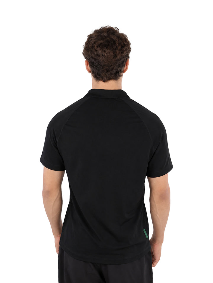 Hombre vistiendo playera polo Lacoste color negro y pantalones negros sobre fondo blanco.
