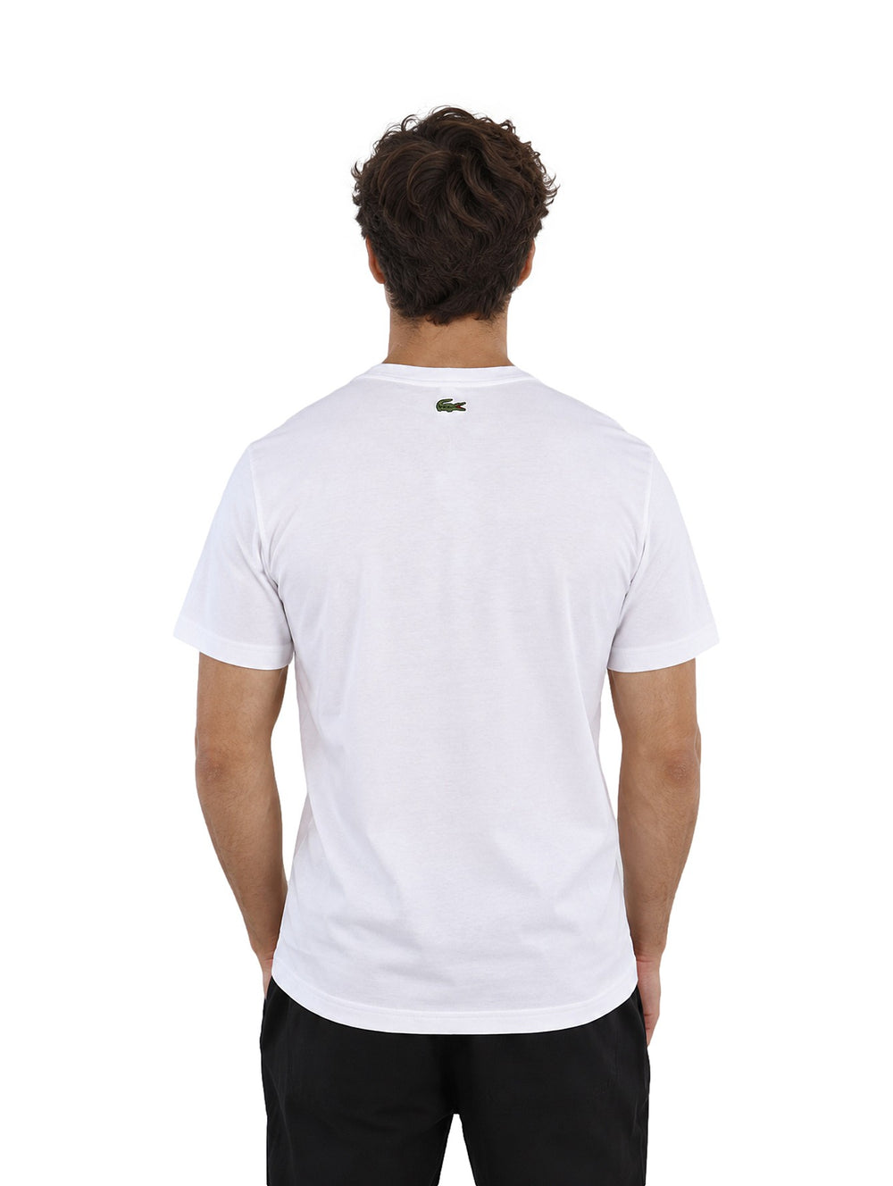 Hombre vistiendo playera blanca de manga corta con logotipo de Lacoste Paris en el pecho.