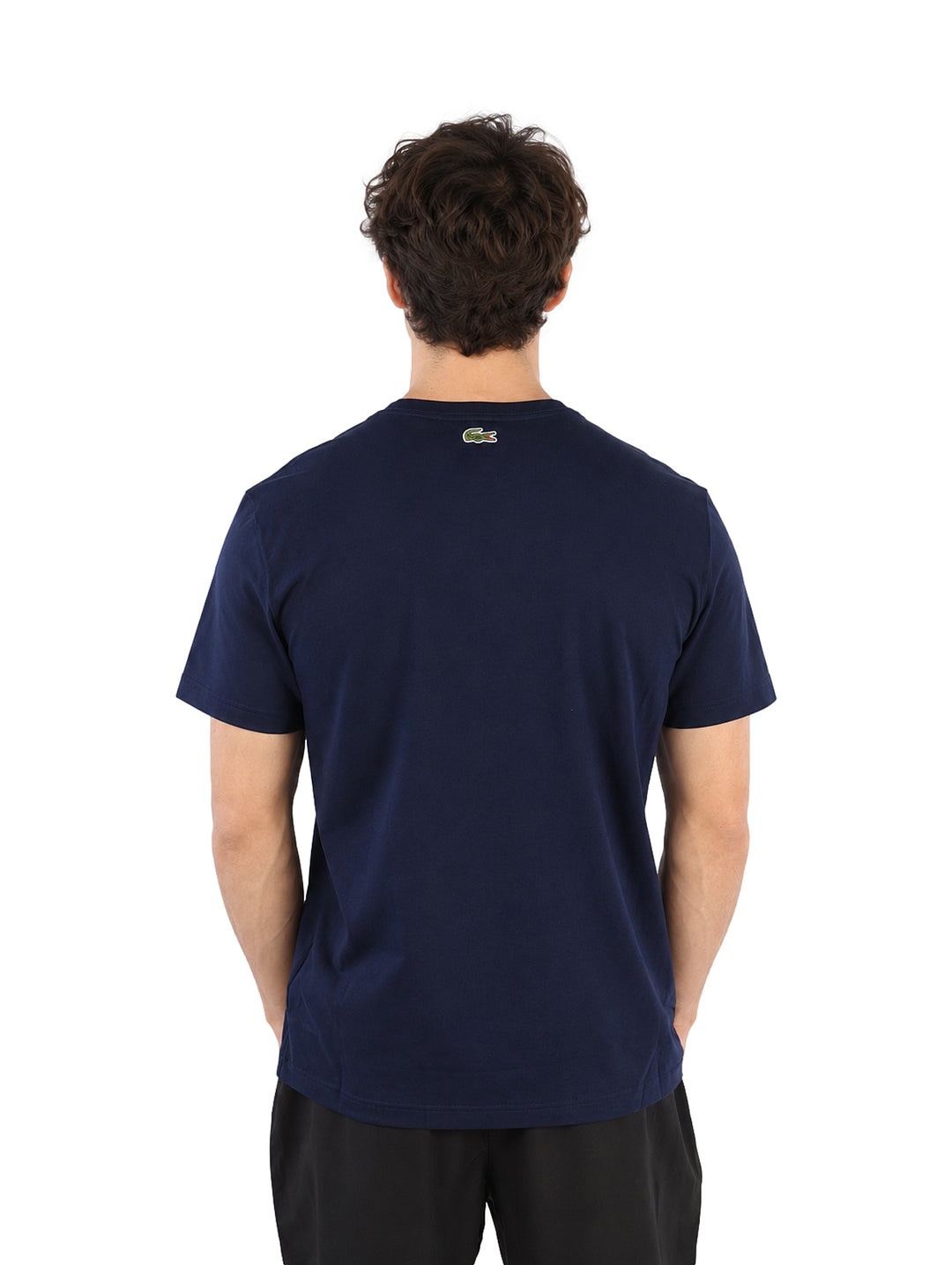 Hombre vistiendo playera Lacoste color navy con logotipo frontal y pantalones negros.