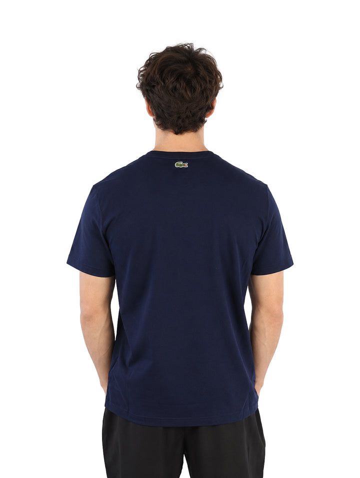 Hombre vistiendo playera Lacoste color navy con logotipo frontal y pantalones negros.