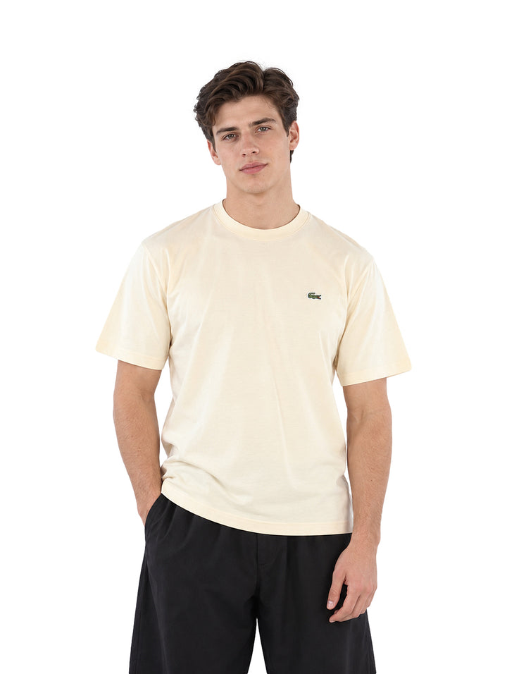 Hombre vistiendo una playera Lacoste color beige de manga corta y cuello redondo.