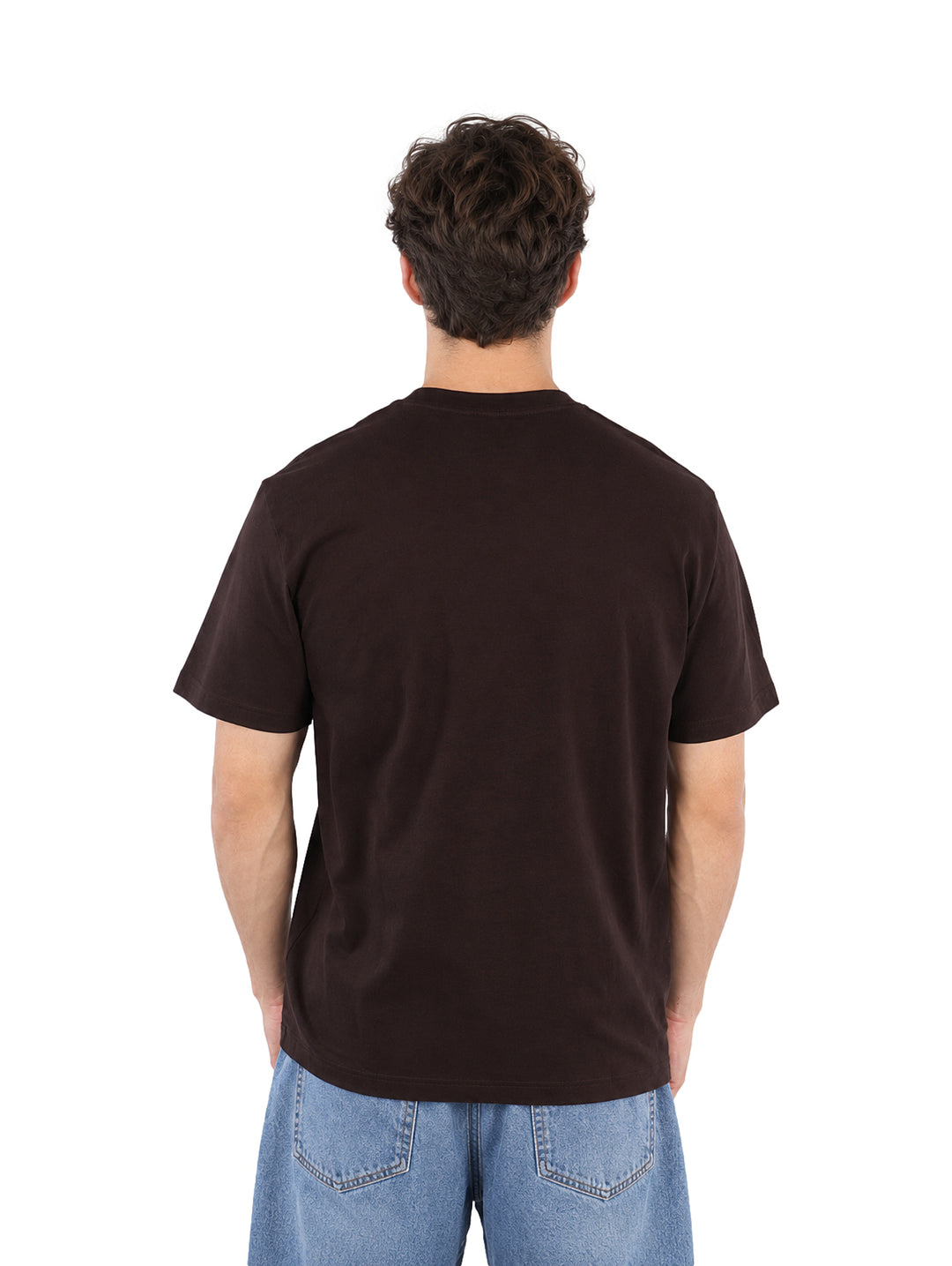 Hombre vistiendo una playera Lacoste de color café y pantalones de mezclilla azules sobre fondo blanco.
