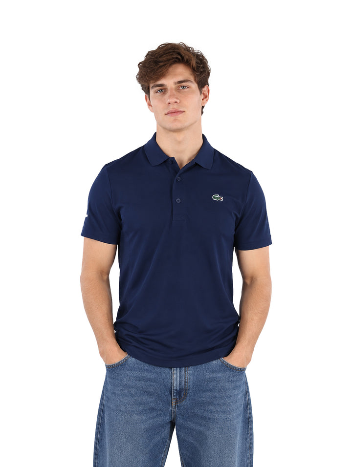 Hombre vistiendo una playera polo Lacoste color azul marino de manga corta.