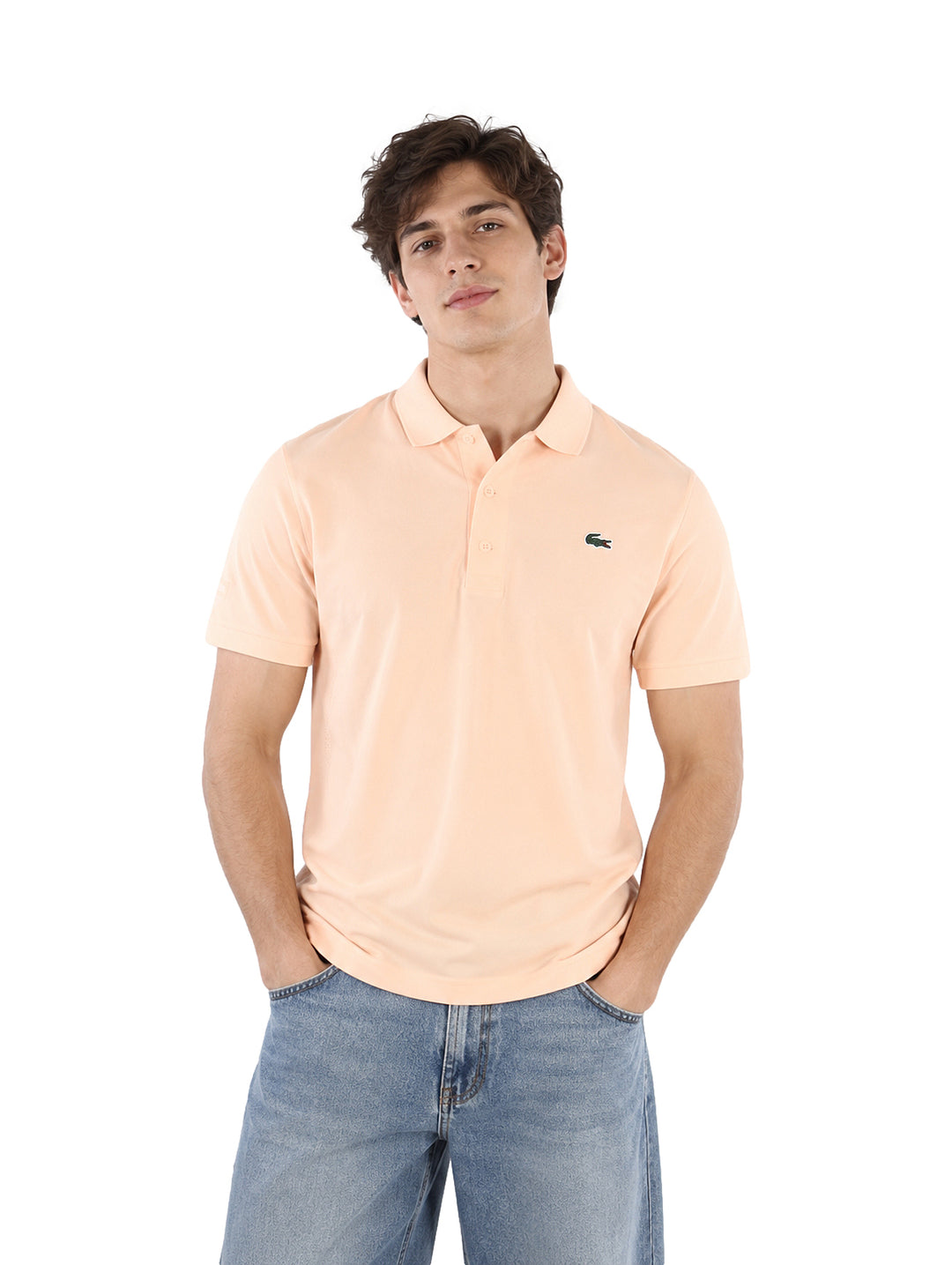 Hombre vistiendo una playera polo Lacoste de color rosa claro y pantalones de mezclilla azules.