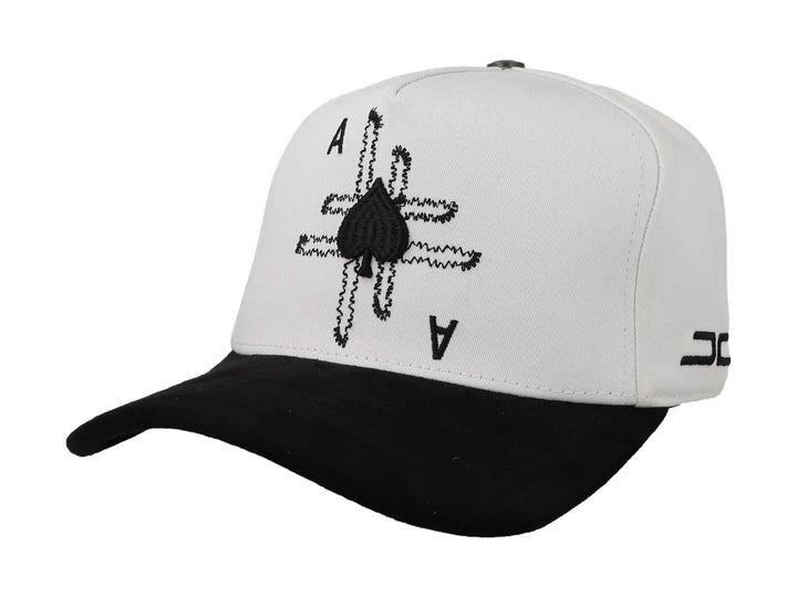 Gorra blanca con visera negra y diseño bordado de as de picas en la parte frontal.