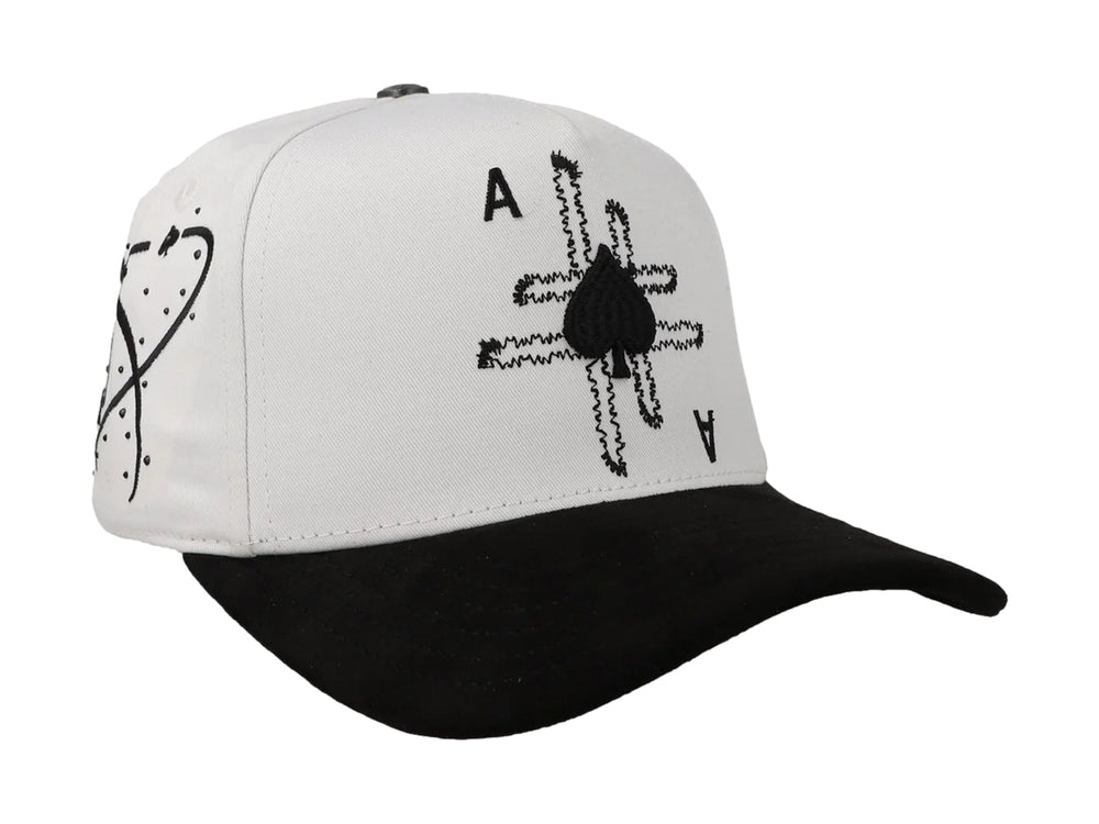 Gorra blanca con visera negra y diseño bordado de as de picas en la parte frontal.