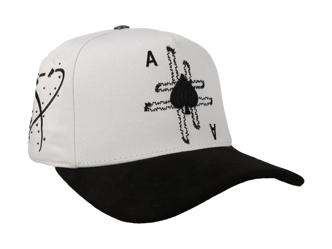 Gorra blanca con visera negra y diseño bordado de as de picas en la parte frontal.