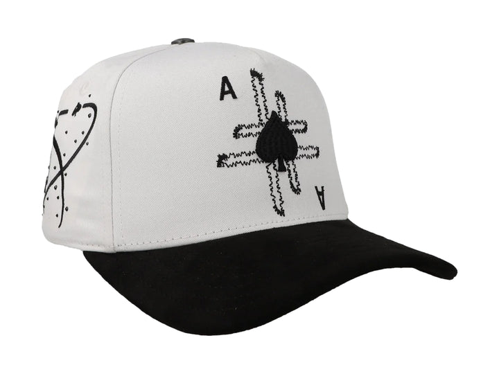 Gorra blanca con visera negra y diseño bordado de as de picas en la parte frontal.