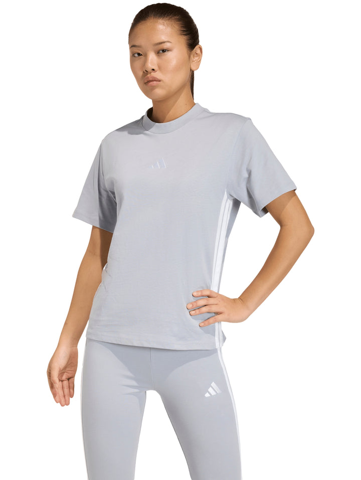 Camiseta deportiva Adidas de color gris claro con tres franjas blancas laterales.