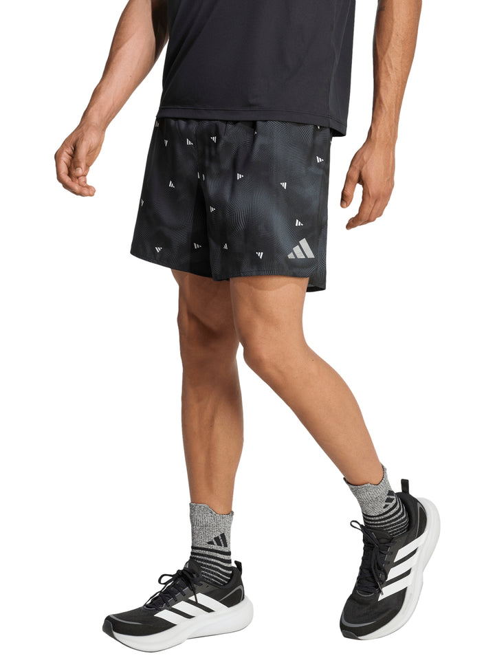 Hombre vistiendo shorts deportivos Adidas color negro con detalles blancos y estampado sutil.