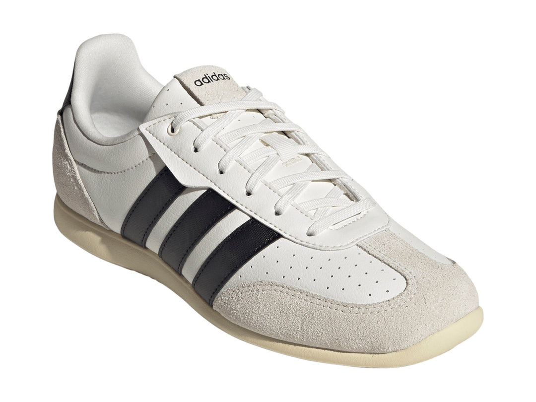 Tenis Adidas blancos con tres franjas negras y detalles en color crema en la punta y el talón.